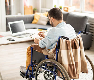 Man in wheelchair working on computer and taking notes